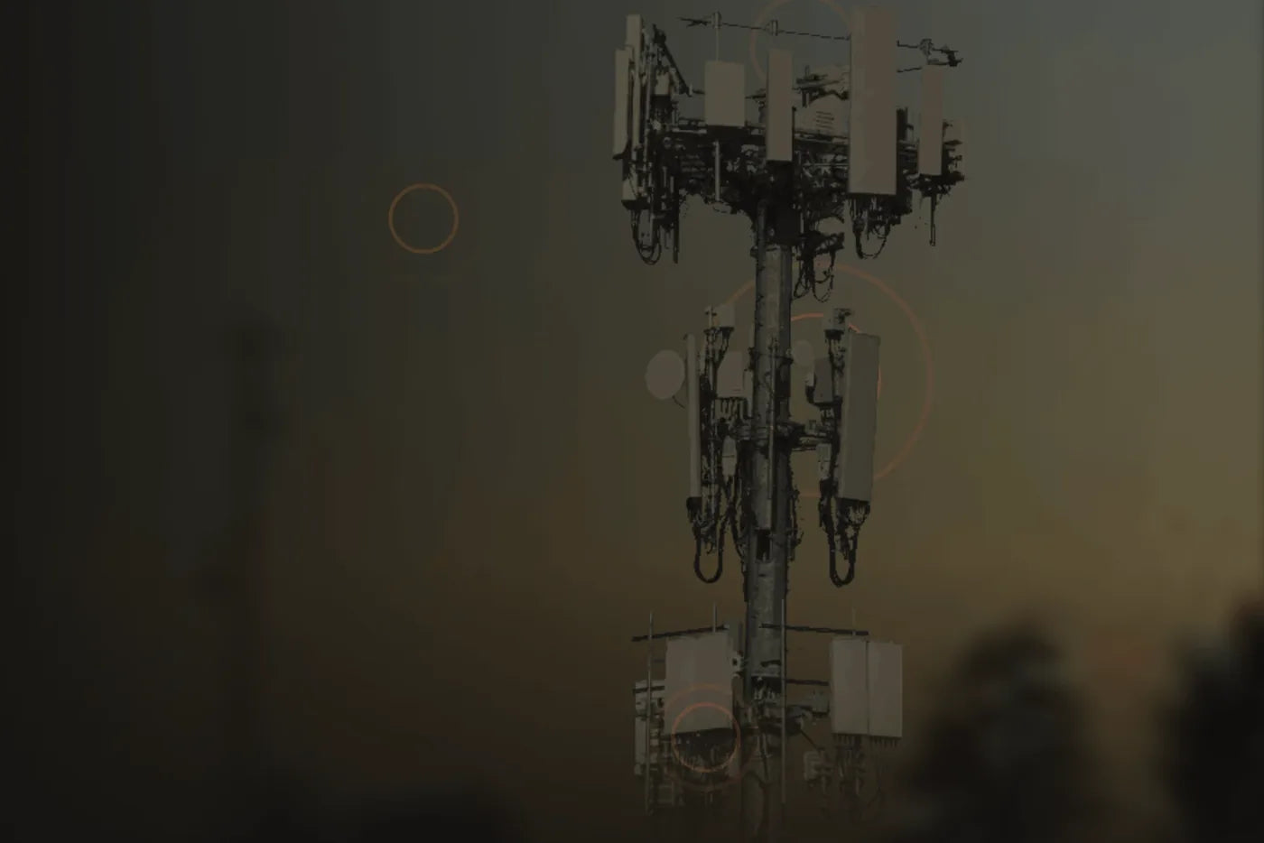 A cell tower against a dusk sky, its antennas picked out in amber