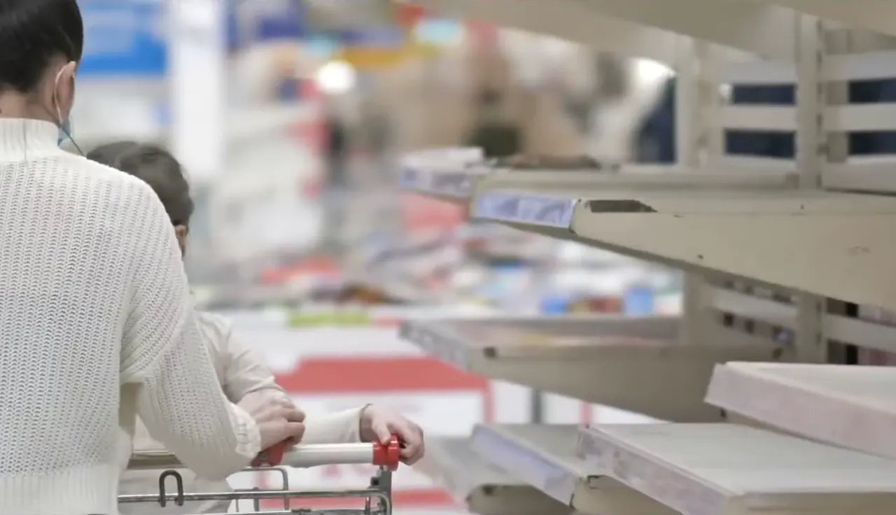 A woman and a child push a shopping cart past empty store shelves